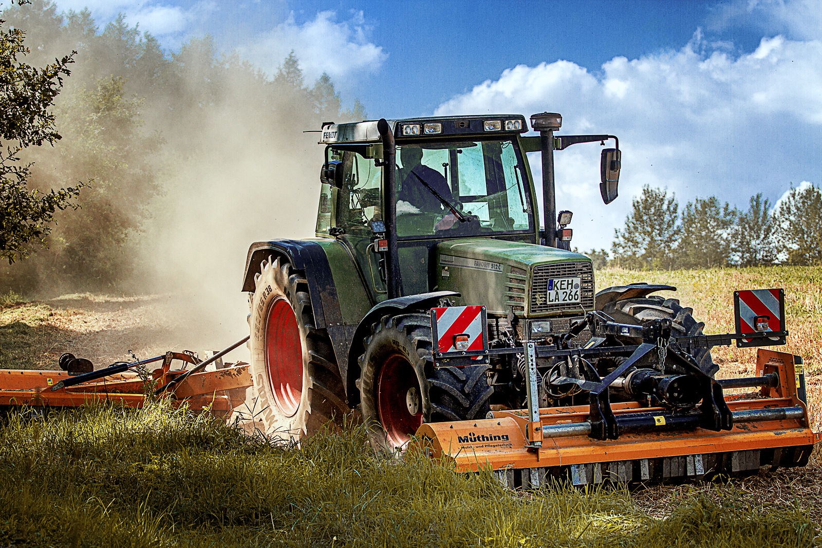 Traktor beim Mulchen mit Staub auf dem Feld