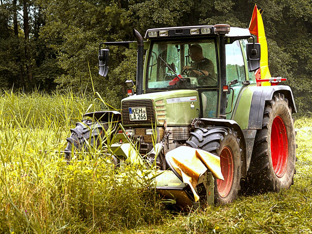 Traktor mit Mähwerk bei der Grünlandarbeit